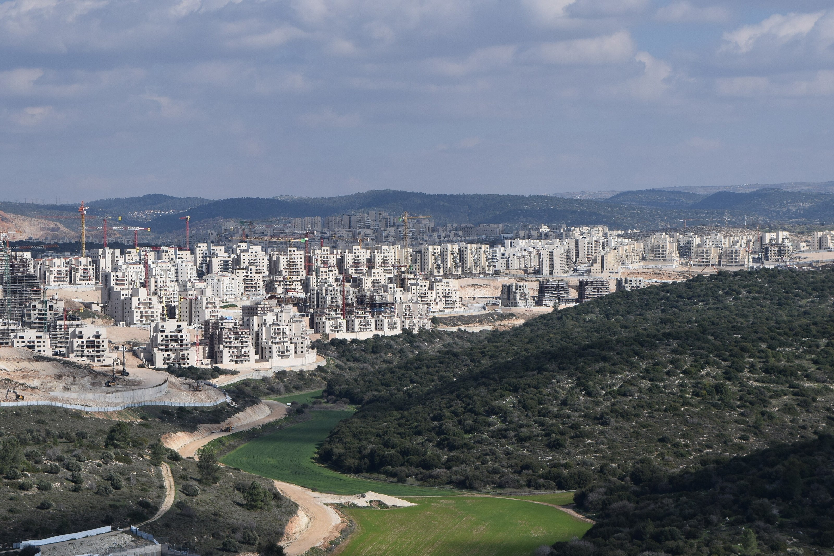 Ramat Beit Shemesh Daled and Gimmel seen from Tel Azekah: rows of new apartment blocks and construction cranes above a wooded valley