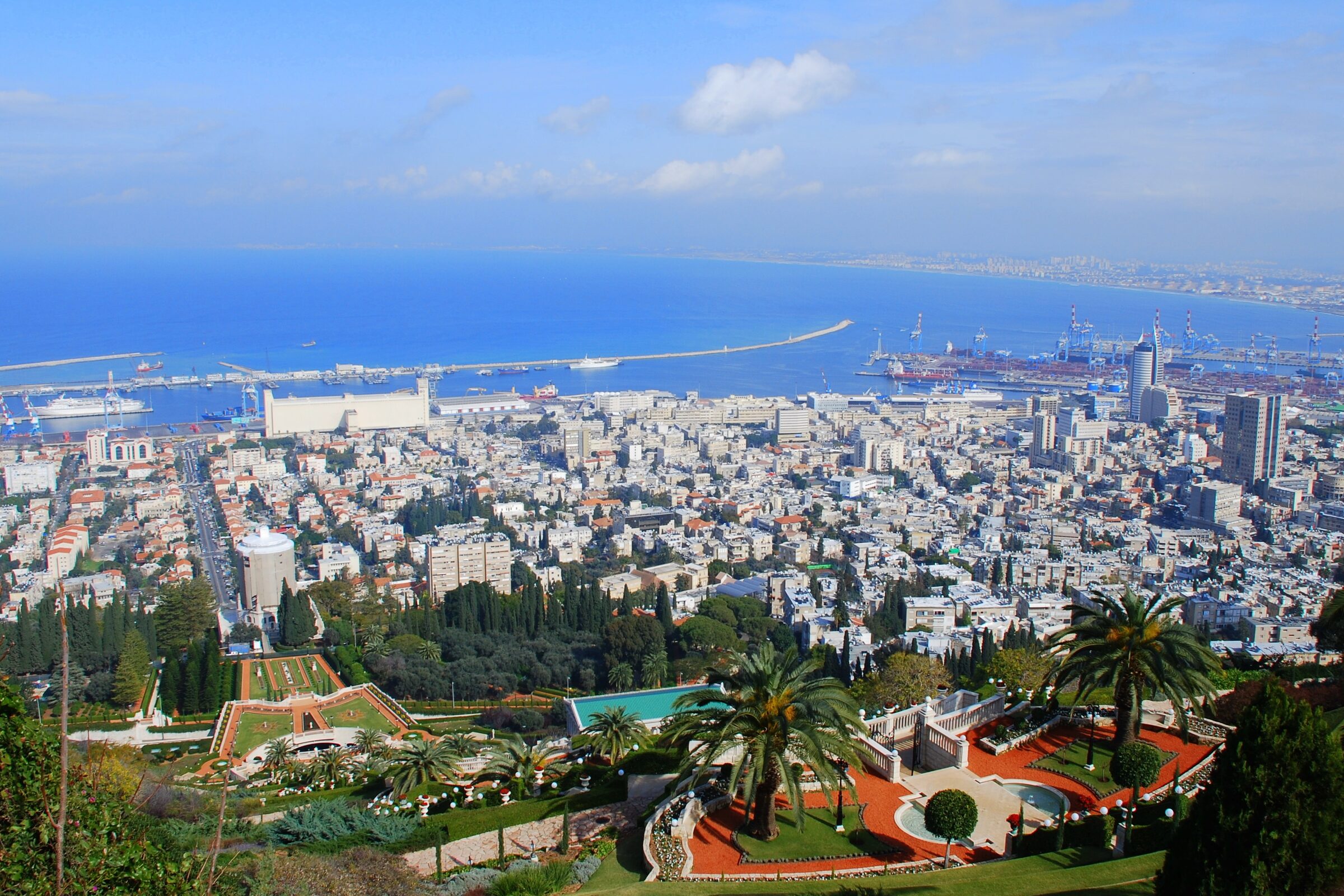 Haifa seen from the slope of Mount Carmel: garden terraces with palms in front, the city's white buildings below, and the port and bay behind