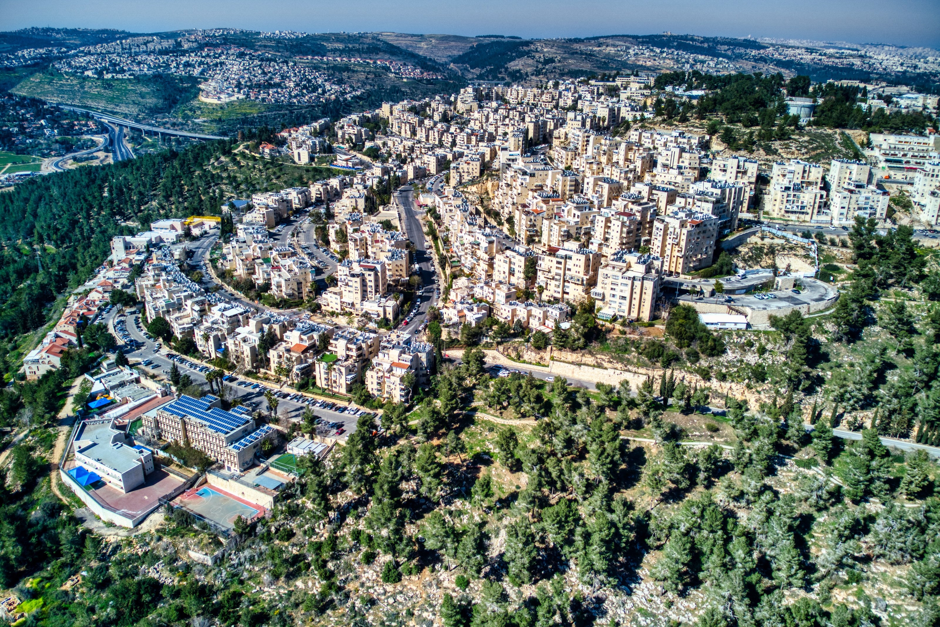 Har Nof from the air: apartment blocks along a curving ridge above a pine forest, Jerusalem