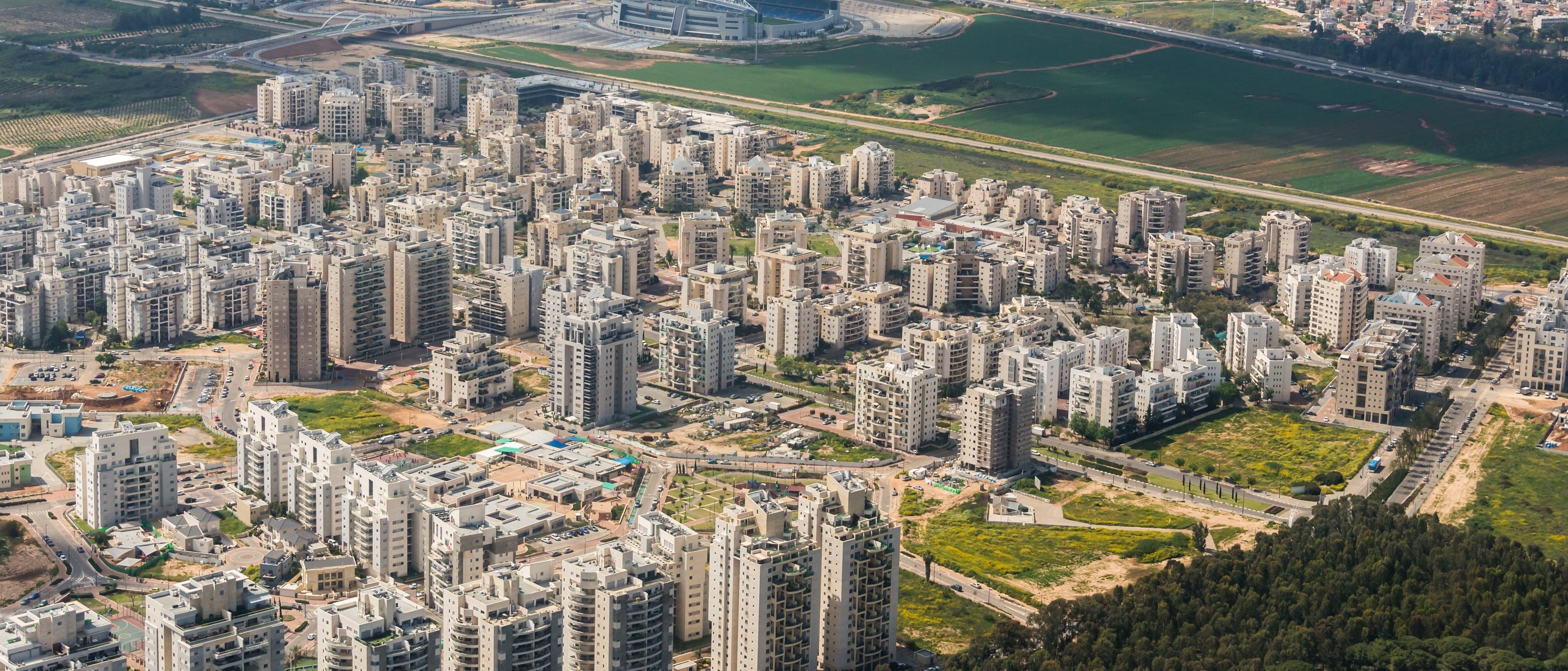 Kiryat Hasharon from the air: streets of new apartment blocks between open fields and a pine wood