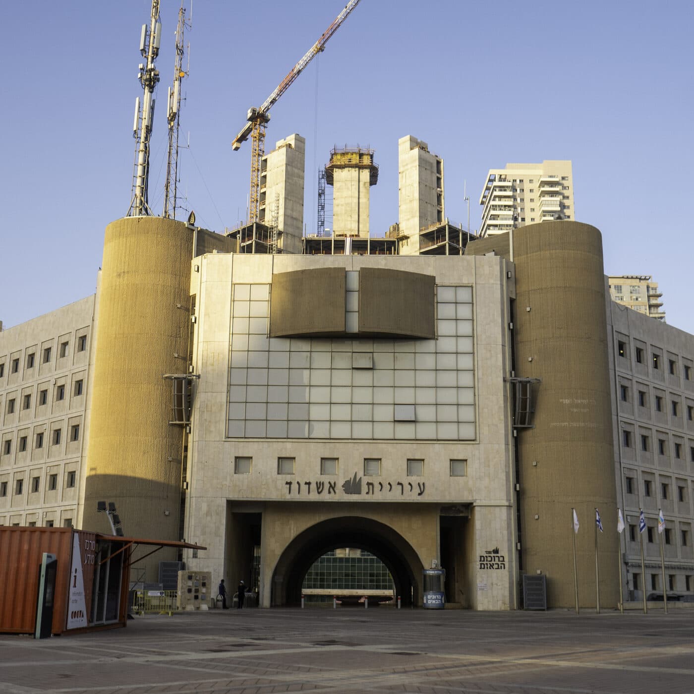 Ashdod City Hall: a pale stone building with two round towers and an arched entrance, a crane and apartment towers behind it