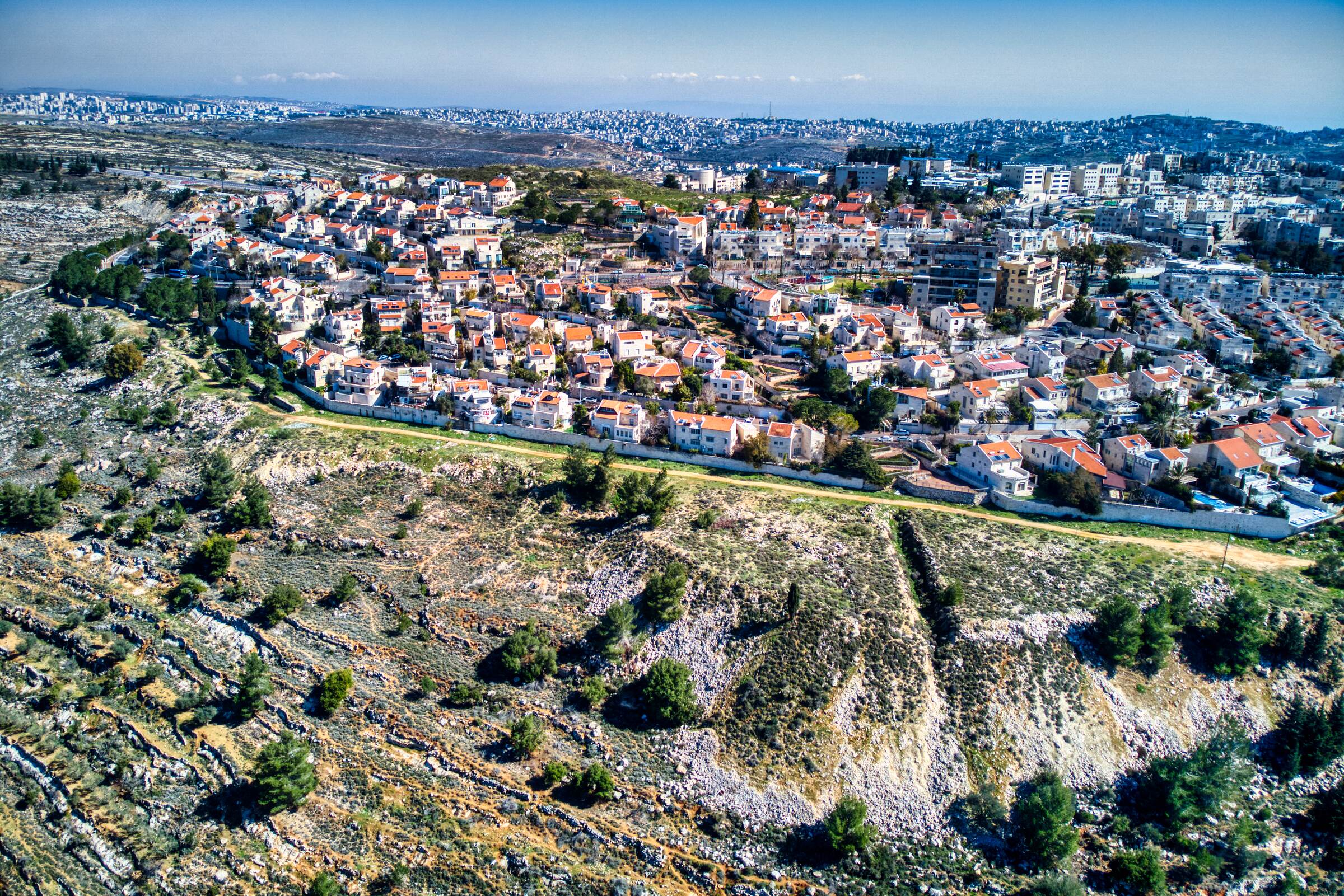 Houses and apartment buildings along the edge of a Ramot ridge, above a rocky terraced slope