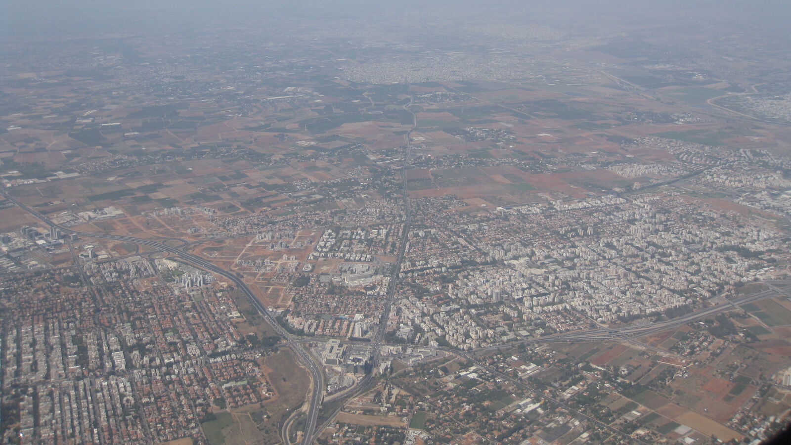Kfar Saba from the air: blocks of apartment buildings and red-roofed houses crossed by a highway interchange, with farmland beyond