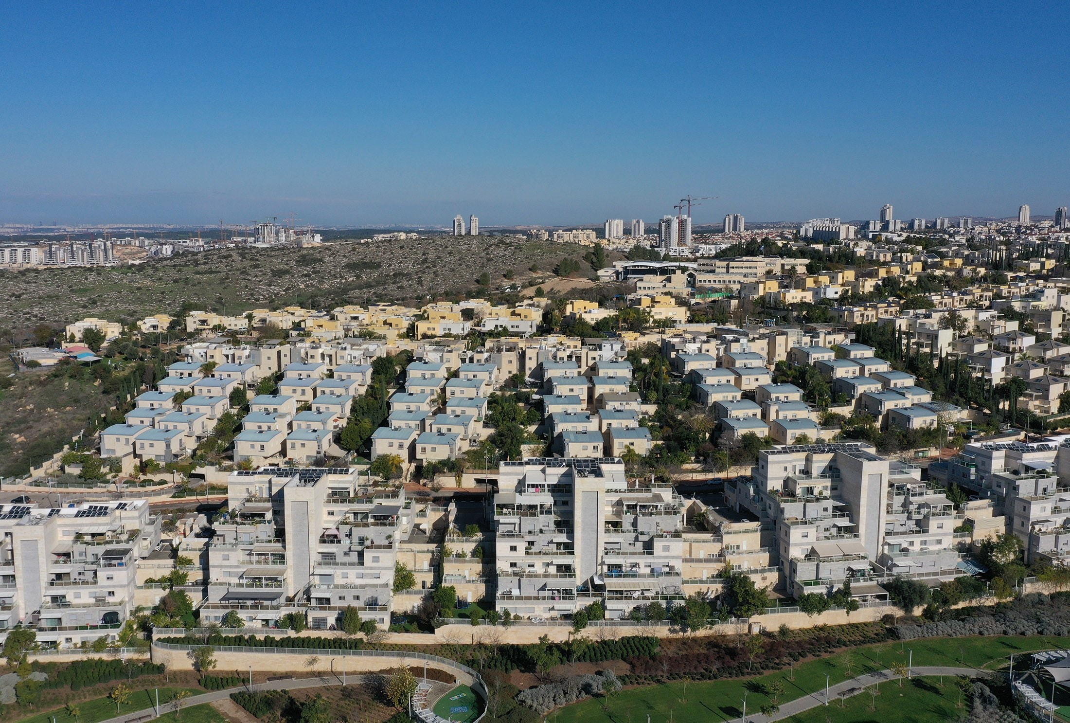 Buchman in Modi'in from the air: rows of terraced apartment buildings and townhouses above a park, the city's towers on the horizon
