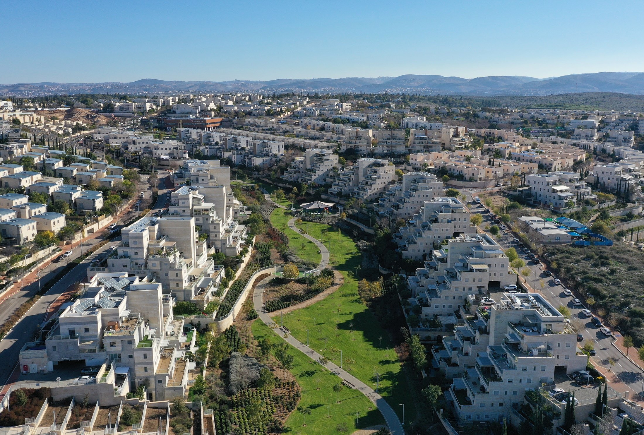 Buchman in Modi'in from the air: terraced stone apartment buildings either side of a green park valley, the Judean hills on the horizon