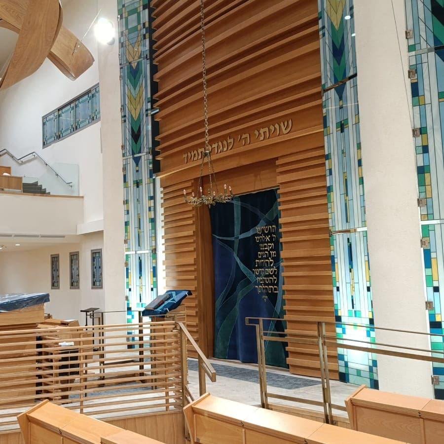 The sanctuary of Kehillat Ohel Ari in Ra'anana: a wooden ark between tall stained glass panels, with the women's gallery above